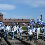 A visitor to Auschwitz carries the Israeli flag as a group examines a boxcar used to transport Jews to extermination and concentration camps.