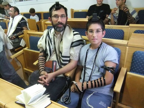 A father and son wear tefillin, which symbolize devotion to God and the Torah, during morning prayers.