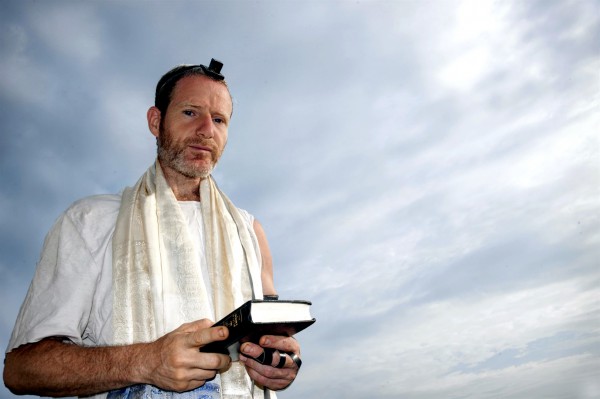 A Jewish man prepares for morning prayer wearing tefillin (phylacteries) and a tallit (prayer shawl).