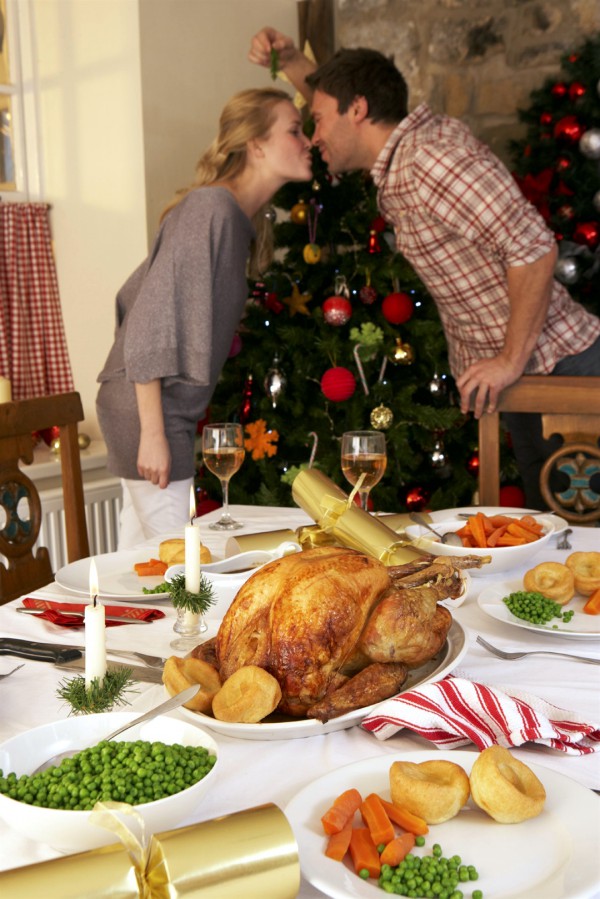 With Christmas dinner on the table, a young couple kisses under the mistletoe.