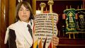 A Jewish teen holds a Torah scroll covered by an ornately decorated Torah mantle that commemorates those who perished in Nazi death camps during the Holocaust.