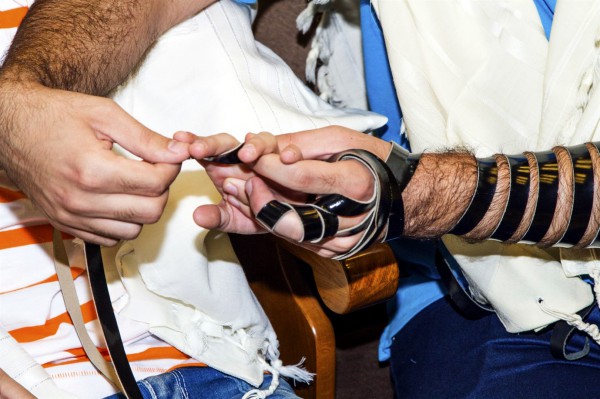 An adult shows a boy how to wind tefillin (phylacteries) around the hand.