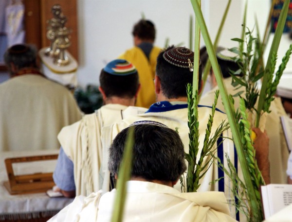 Jewish men pray in a synagogue on Sukkot. They are holding Sukkot's Arba'ah Minim (Four Kinds of plant), which are mentioned in Leviticus 23:40.