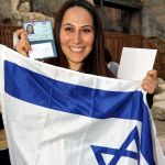 A woman holds up the Israeli flag and her new Israel identification after making Aliyah. (Jewish Agency photo by Brian Hendler)