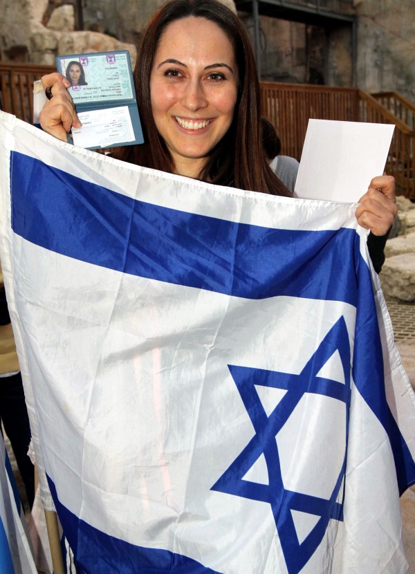 A woman holds up the Israeli flag and her new Israel identification after making Aliyah. (Jewish Agency photo by Brian Hendler)