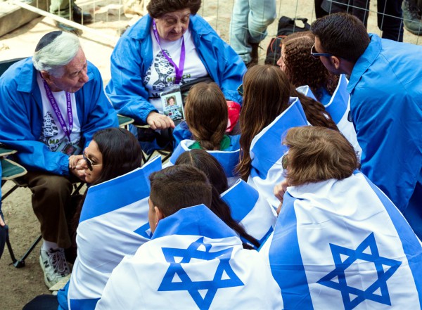 Teens wrapped in Israeli flags at the Auschwitz extermination camp listen to the testimony of Holocaust survivors.