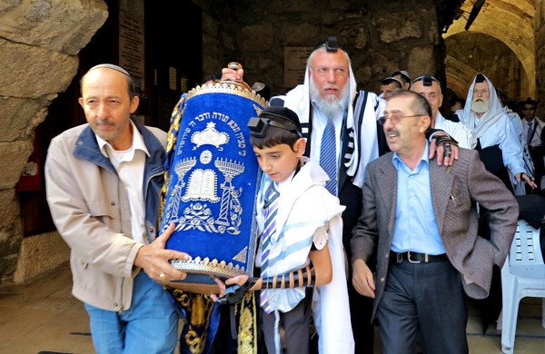 A Jewish father and son at the Western (Wailing) Wall in Jerusalem share the burden of carrying the heavy Torah scroll.