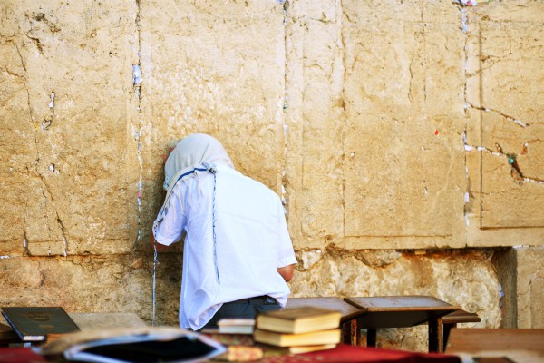 A Jewish man prays at the Western (Wailing) Wall with his tallit (prayer shawl) pulled over his head.