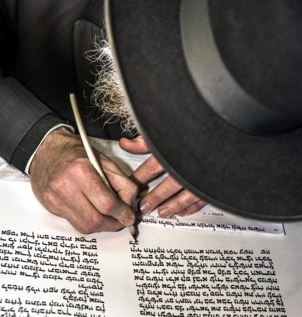 A Jewish scribe hand writes a Torah scroll.