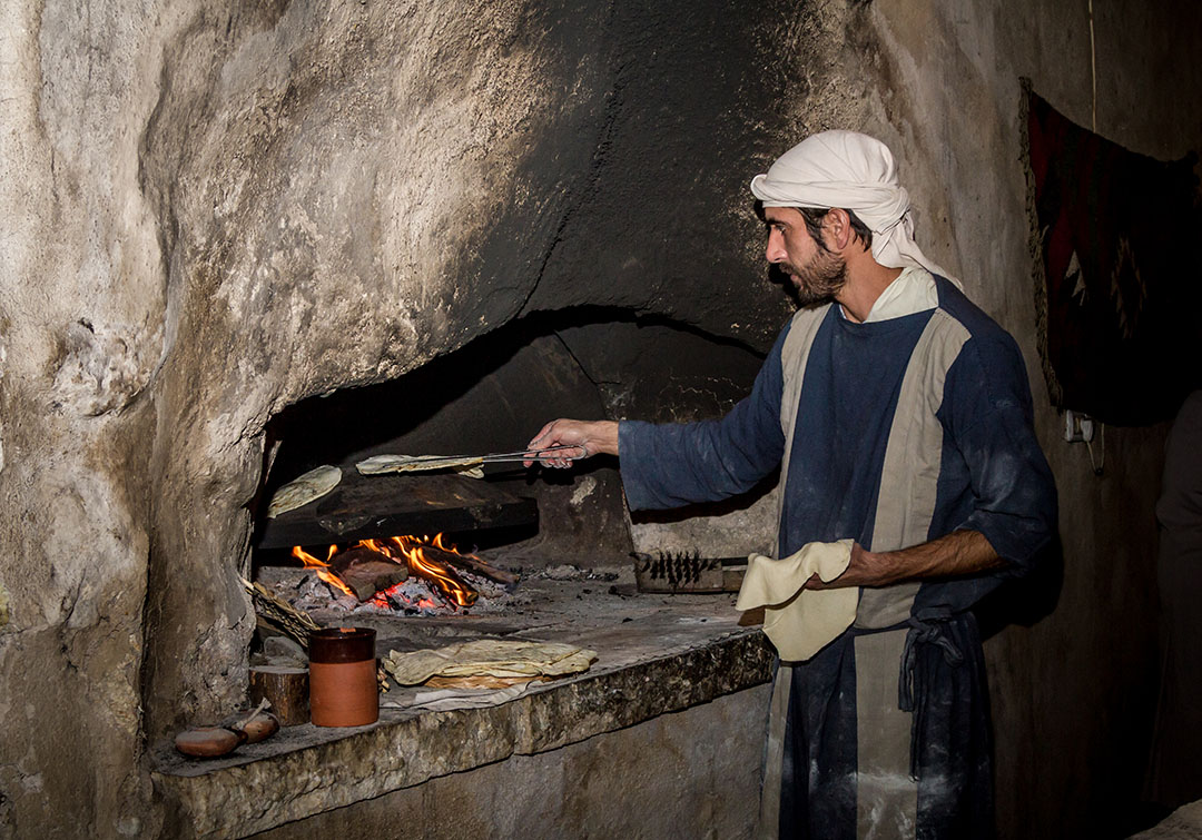 Man bakes bread at a recreated home in Nazareth, wearing period clothes from the time of Yeshua.