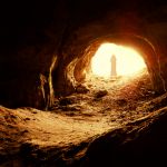 Man standing at entrace of cave looking out.